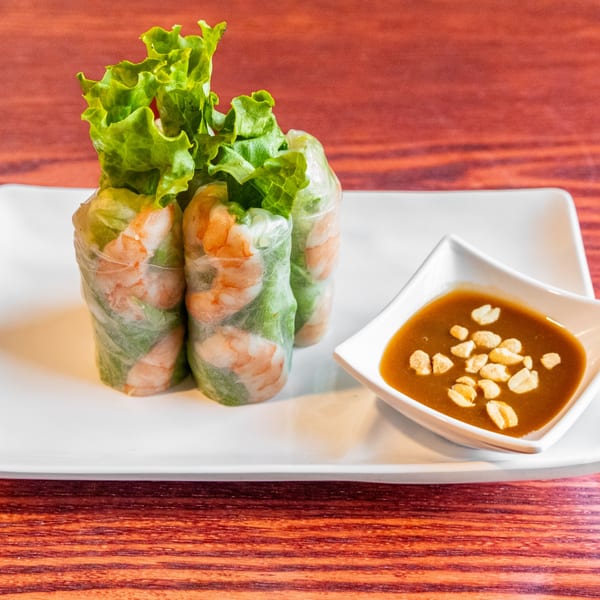 Three fresh Vietnamese shrimp spring rolls with lettuce and peanut dipping sauce on a white plate.