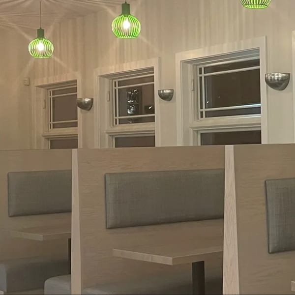 Interior of Saigon Cafe with light wood booths, gray upholstery, and green pendant lights.