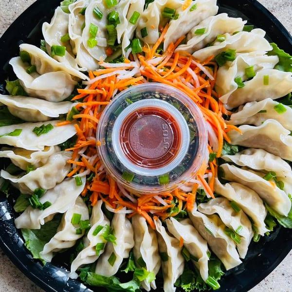A platter of steamed dumplings garnished with green onions, shredded carrots, and a dipping sauce.