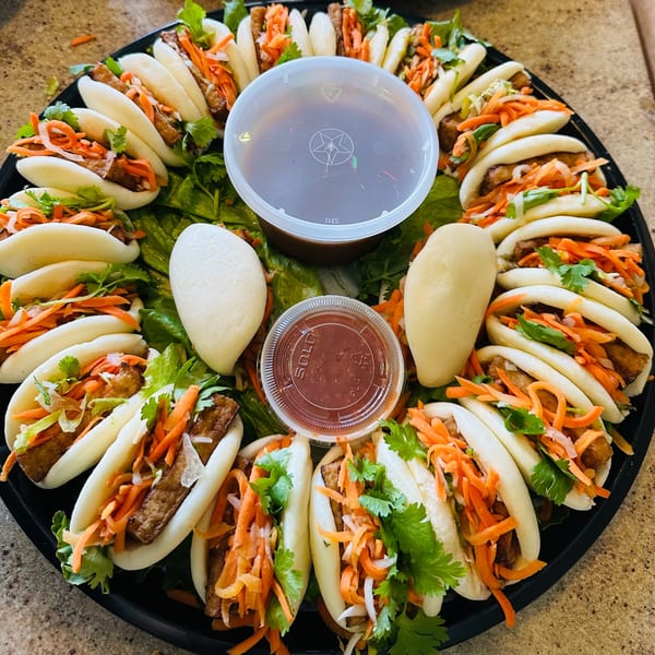 A platter of Saigon Cafe's Vietnamese bao buns filled with meat, carrots, and cilantro, with dipping sauces.