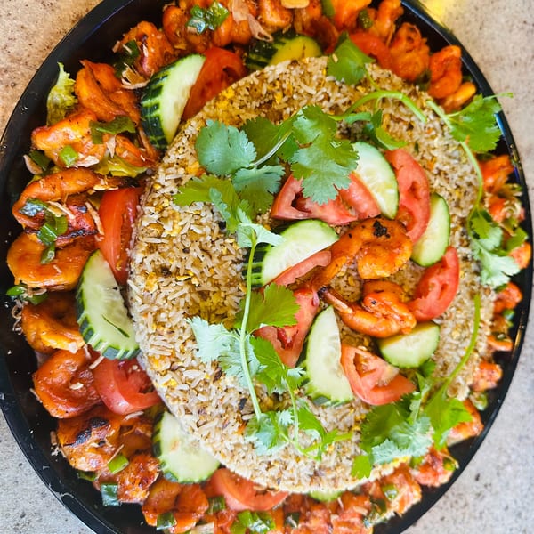 A large platter of Vietnamese fried rice surrounded by grilled shrimp, sliced cucumbers, and tomatoes.