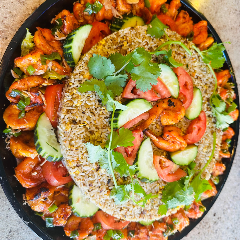 A large platter of Vietnamese fried rice surrounded by grilled shrimp, sliced cucumbers, and tomatoes.