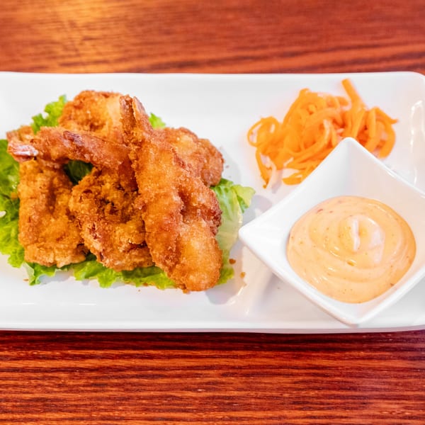 Crispy fried shrimp on lettuce with shredded carrots and a creamy dipping sauce on a white plate.
