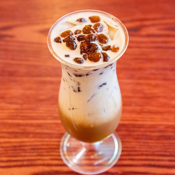 A tall glass of Vietnamese bubble tea with tapioca pearls and ice on a wooden table.