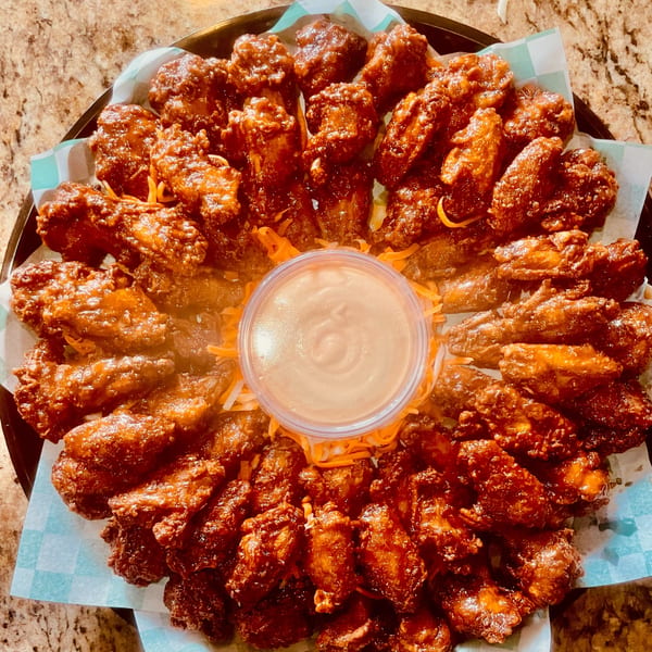 A platter of Saigon Cafe's glazed chicken wings with shredded cheese and a dipping sauce.