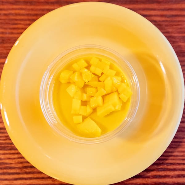 Mango pudding dessert with diced mango pieces in a clear cup on a yellow plate.